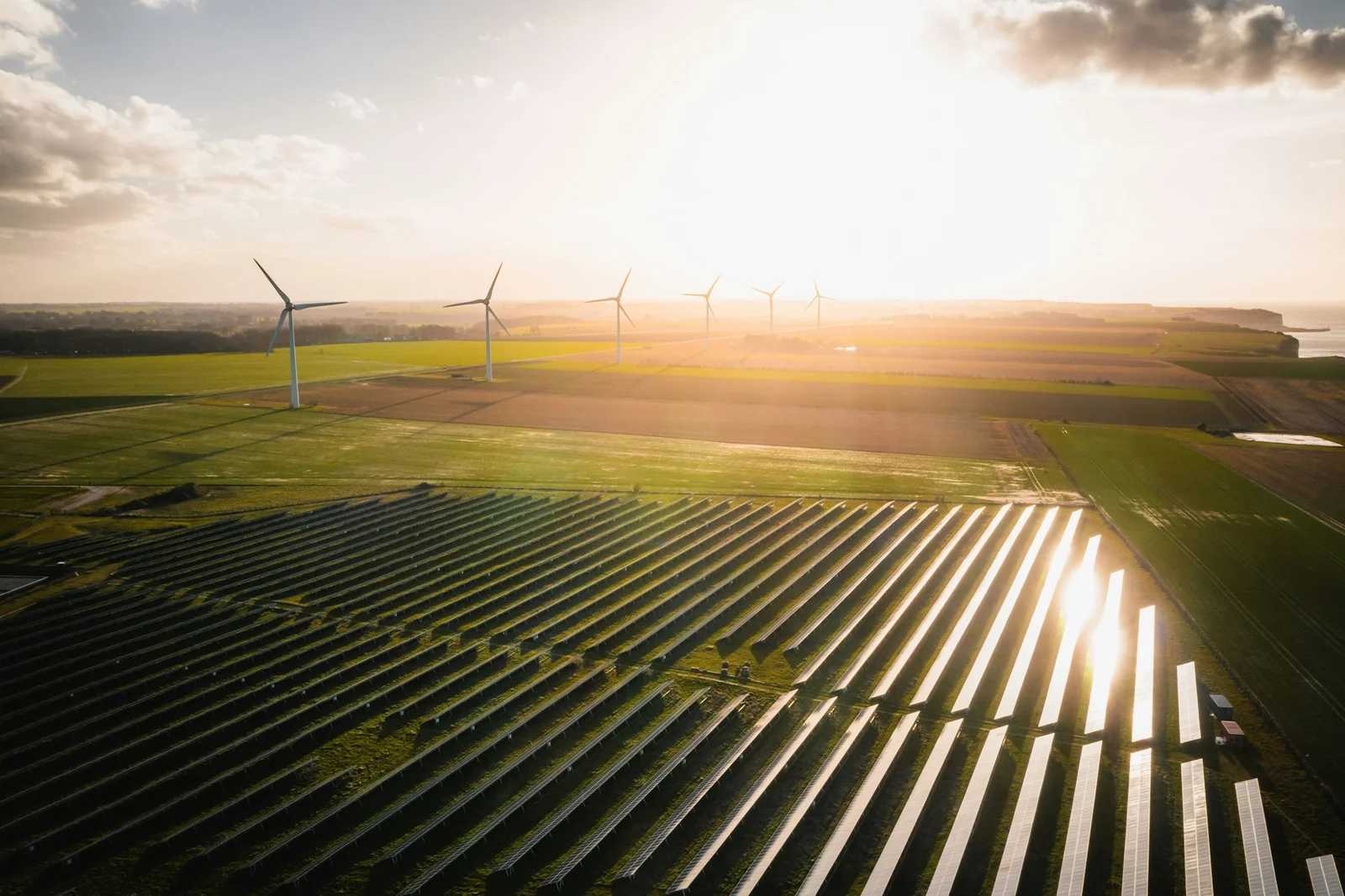 日落時從高處俯瞰的太陽能發電場,後方有風力發電機,象徵 AI 由產生內容逐步走向參與企業營運