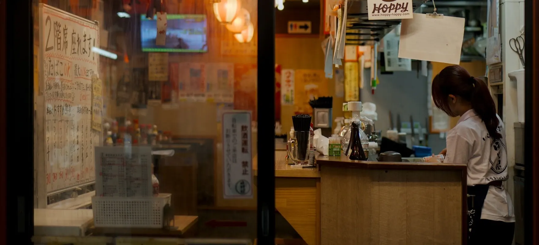 A staff member preparing orders behind the counter of a busy izakaya